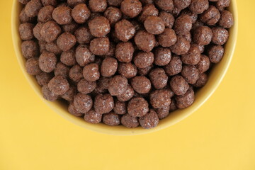 Chocolate cereal corn balls in a yellow bowl on a yellow background. Top view. Copy, empty space for text