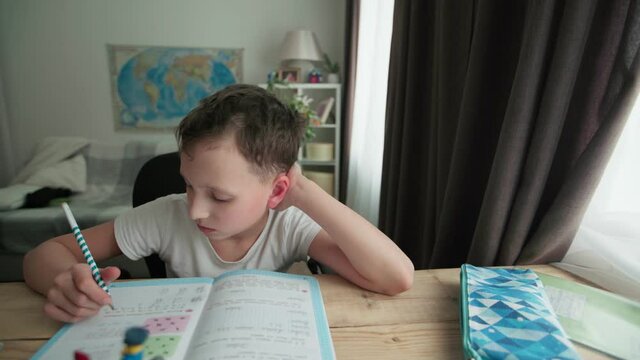a capable student of 8 years old, writes in a notebook at the table.  the boy is doing his homework. Home schooling.