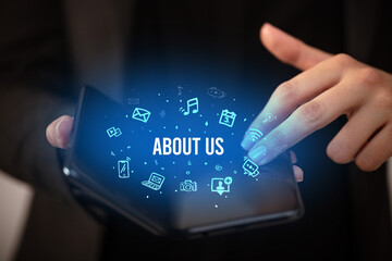 Businessman holding a foldable smartphone with ABOUT US inscription, social media concept