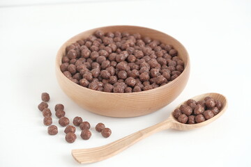Chocolate corn balls in a wooden bowl and spoon scattered on a white background. Top view. Copy, empty space for text