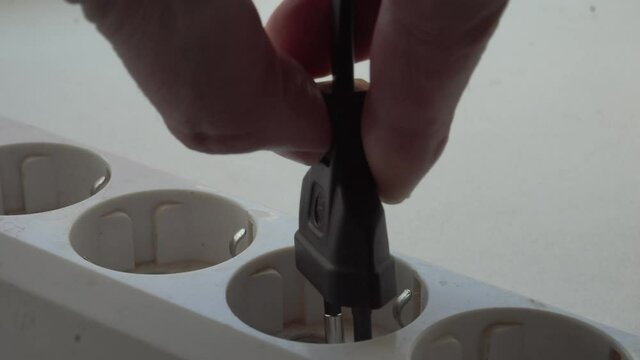 The man takes a black electric plug with a cord from the electrical appliance and sticks it in a nearby socket