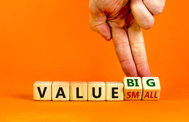 Small or big value symbol. Businessman turns wooden cubes and changes words 'value small' to 'value big'. Beautiful orange background, copy space. Business and small or big value concept.