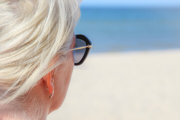 kobieta w okularach przeciwsłonecznych o bląd włosach wpatrująca się w morze