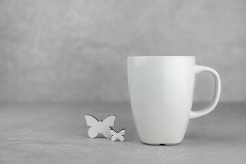 Fototapeta na wymiar Blank white mug mockup with white butterfly on light concrete stone background. Spring composition. Side view. Copy space.
