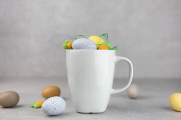 Blank white mug mockup with colorful easter eggs and carrots, light concrete stone background. Spring composition. Side view. Copy space.