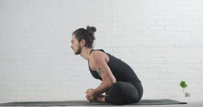 Young man practicing yoga, sitting in Butterfly exercise, baddha konasana pose with forward bend, working out, wearing sportswear, indoor, at floor