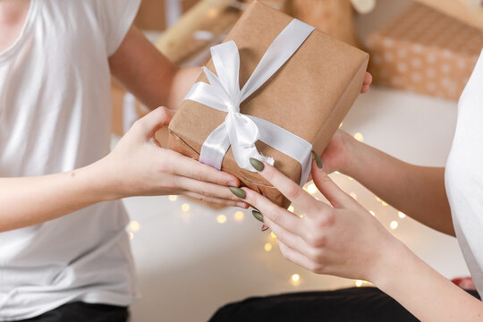 Cropped photo of Young man giving a gift box to his surprised happy woman. party moment. Hands of young boyfriend surprise in box with white ribbon to his girlfriend.