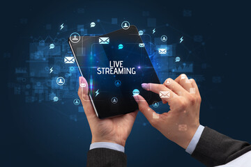 Businessman holding a foldable smartphone with LIVE STREAMING inscription, social networking concept