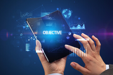 Businessman holding a foldable smartphone with OBJECTIVE inscription, successful business concept