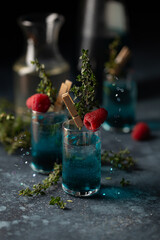 Set of cocktails in shot glasses with blue liqueur,thyme sprigs and fresh raspberry.Close up of blue drink.