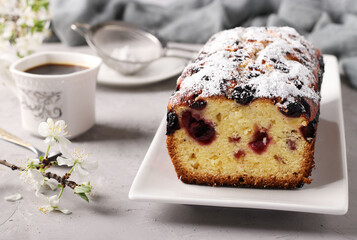 Cupcake with cherries on a white plate on light gray background and a cup of coffee. Closeup
