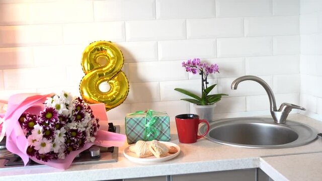 Bouquet of spring flowers and golden ballon 8 eight on kitchen table with gift box and breakfast. Light scandinavian style. Mothers Day. March 8, International Women's Day