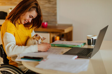 Beautiful girl in wheelchair studying at home with a cat