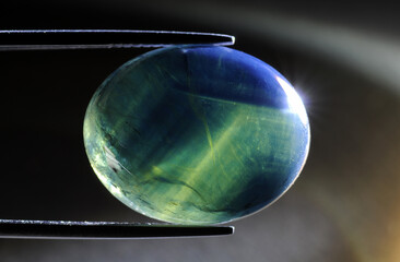 natural star sapphire cabochon gemstone close up front photo in tweezers. Look inside massive crystal of stone stucture, inpurities, inclusions, crystal grow pattern lines, diffusion treament marks