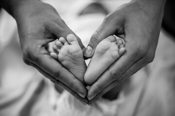 Newborn baby feet in its mother's hands shaped like a heart. Mother showing her love and affection. Black and white