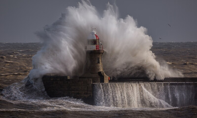 Fototapeta na wymiar Giant waves batter the 15metre tall lighthouse which guards the south pier at the mouth of the Tyne at South Shields, England