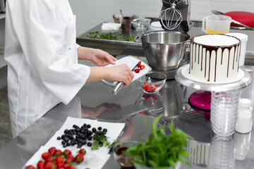 Obraz na płótnie Canvas Pastry chef cuts strawberries to decorate the cake