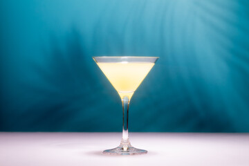 Refreshing pineapple cocktail with slice of pineapple and mint in front of shadow of palm leaves in a shining sun.