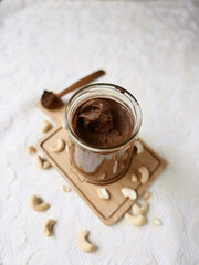 A still life with a homemade raw chocolate cashews butter on a white background. Food background of a cashews spread glass jar, milk chocolate and cashews on spoon. Top view.