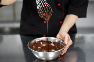 Pastry chef whips melted chocolate in a bowl with a metal wire whisk close up