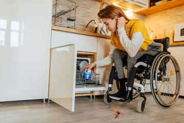 Woman in wheelchair using dishwasher - obrazy, fototapety, plakaty