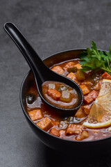 Soup with tomato, lemon and meat in a plate with a spoon