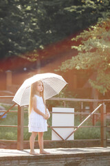 Fototapeta premium A beautiful girl of six years old in a short white dress stands on the masonry near the river and holds a white umbrella in her hands
