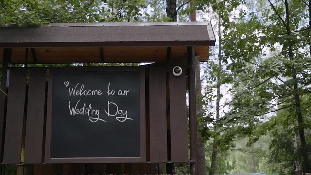 Wedding invitation is written in white chalk on slate plate board on wooden wall in forest. Welcome to our wedding.