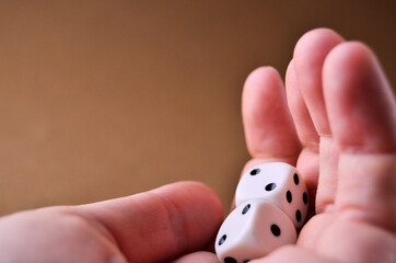 White dice lie in the palm of your hand close up on a brown background with a copy space. High quality photo