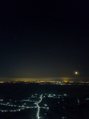 Fototapeta premium Distant lights of the night city under the starry sky. Aerial drone view. Winter frosty night.