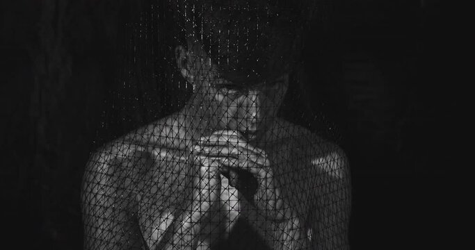 Human trafficking. Kidnapping crime. Forced labour. Violence slavery. Defocused black and white portrait of scared terrified hurt humiliated shirtless guy isolated in mesh trap on dark background.