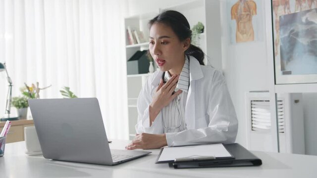 Young Asia lady doctor in white medical uniform with stethoscope using computer laptop talking video conference call with patient at desk in health clinic or hospital. Consulting and therapy concept.