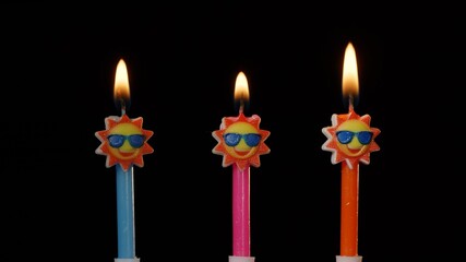 Birthday funny candles in form of sun in sunglasses isolated on black background. Anniversary celebration concept, making a wish. Three festive cake candles burning close-up, macro