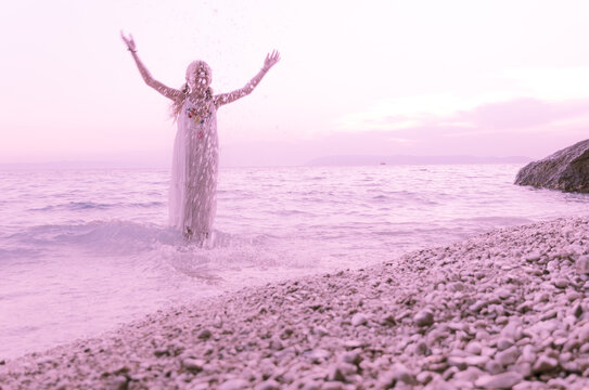 child splashing water while standing in the sea at the pubble beach, weird pink purple atmosphere, standing alone and waiting