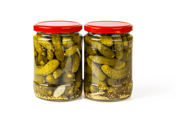 Two full glass jars of pickled gherkins isolated on a white background. Whole green cornichons...
