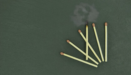 Cinco fósforos novos pousados numa pedra de lousa e um fósforo apagado a fumegar, o fosforo...