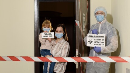 Medical worker in protective suit with inscription text on paper opening entrance door. Sick young family of woman with child daughter girl stay at home during coronavirus covid-19 quarantine lockdown