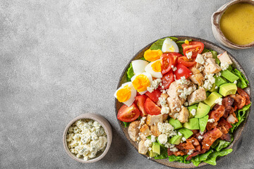 Fototapeta na wymiar Healthy cobb salad with chicken, avocado, bacon, blue cheese, tomato and eggs on gray background. Keto diet food. Top view