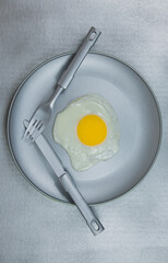 Fried eggs with dark gray plate and cutlery on gray background.