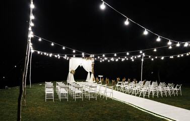 beautiful night stage for the wedding ceremony. wedding wooden arch. stylish wedding decor. chairs for the wedding ceremony. decorative bulbs illuminate the site. empty wedding venue