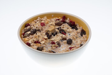 Breakfast oatmeal with nuts and dried fruits in yellow bowl with milk on white background