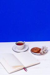 A cup of tea, a notebook and oatmeal cookies. Snack while studying. Education. Homework at school and university. Blue background