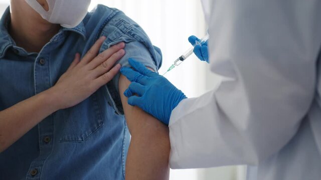 Young Asia lady doctor giving Covid-19 or flu antivirus vaccine shot to senior male patient wear face mask protection from virus disease at health clinic or hospital office. Vaccination concept.