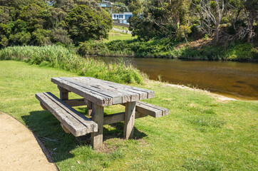 A weathered picnic table at the riverbank of Wye River with some modern houses in the distance. Wye River is a popular travel destination and a coastal town on the Great Ocean Road. VIC Australia.