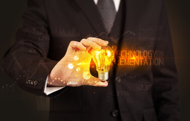 Businessman holding lightbulb with TECHNOLOGY IMPLEMENTATION inscription, Business technology...