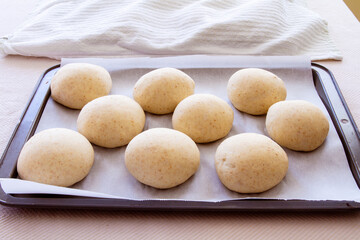 Buns rising before baking on a pan; fresh homemade buns ready to be put into the oven