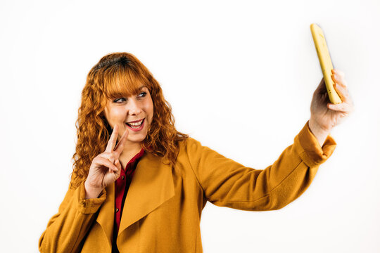 Closeup Shot Of A Redhead Woman With Yellow Coat Taking A Selfie On An Isolated White Background