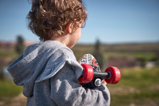 A Baby Girl's Back View With A Mini Skateboard Under Her Arm In The Park