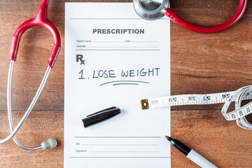 Flat lay image of a physician desk with a stethoscope, a pen, a tape measure, and a prescription that says Lose weight. Getting in shape, doctor recommendation, healthy lifestyle, weight loss concepts
