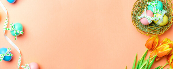 Easter bunny. Colourful egg with tape ribbon, spring tulips, feathers on pastel pink background in Happy Easter decoration. Traditional banner in top view.